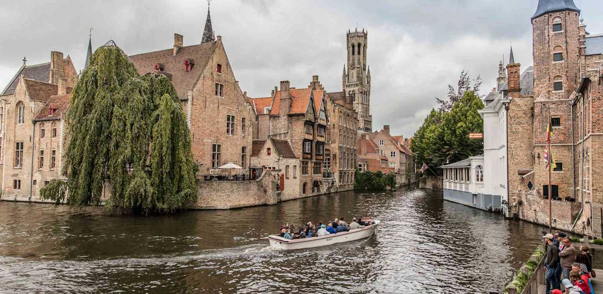 A scenic view of a canal in Bruges with a tourist boat navigating between historic brick buildings.