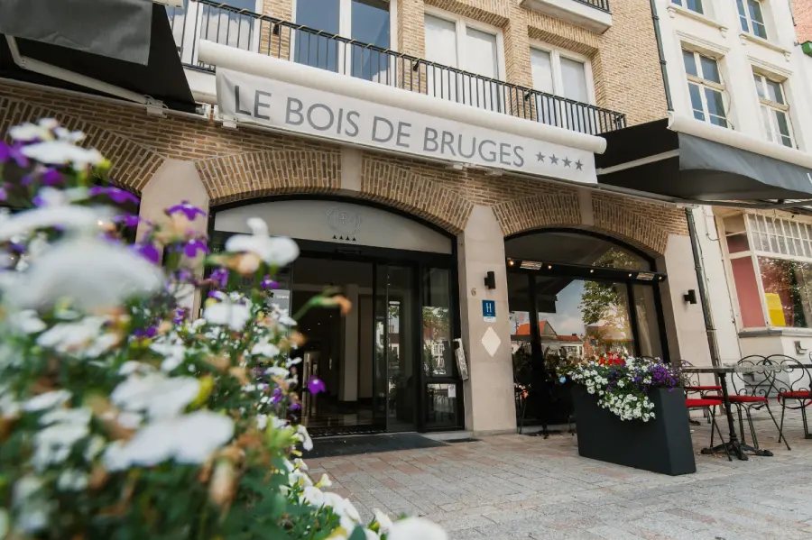 Exterior of Hotel Le Bois de Bruges, a 4-star hotel with a brick facade, arched entrance, and flower planters on the pavement